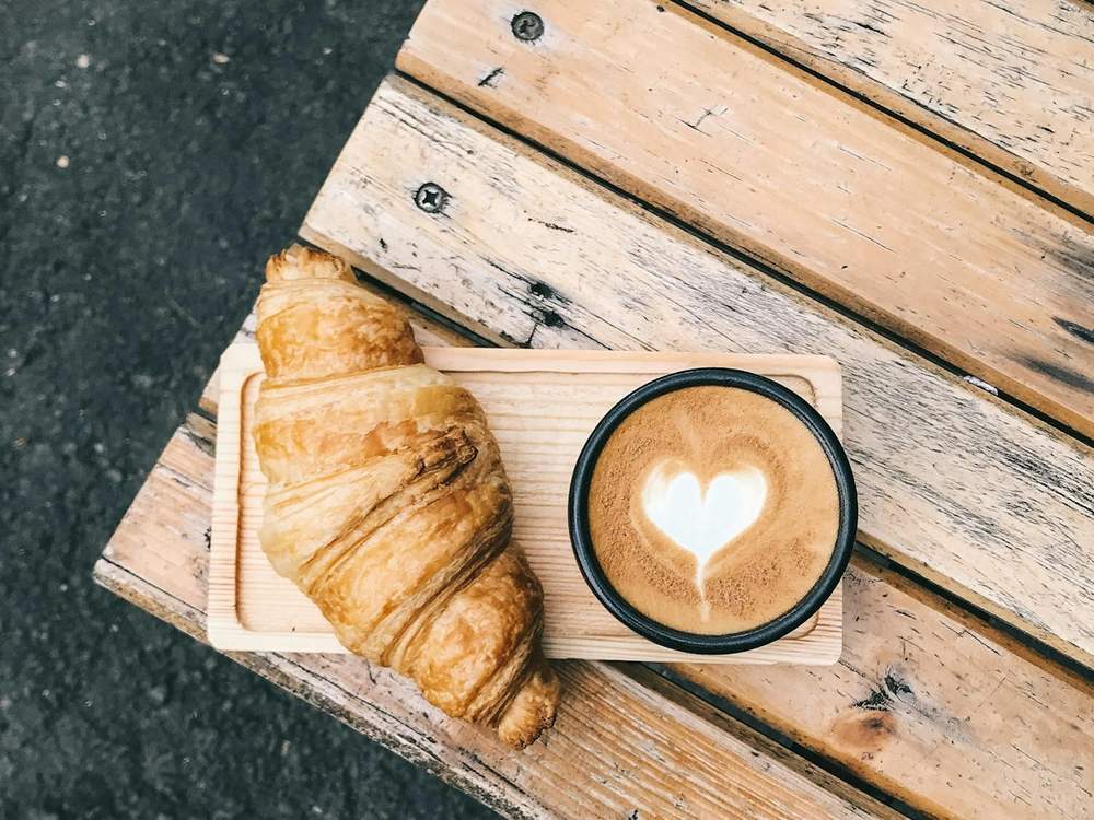 Kroasan i kafa s latte art srcem na drvenom stolu
