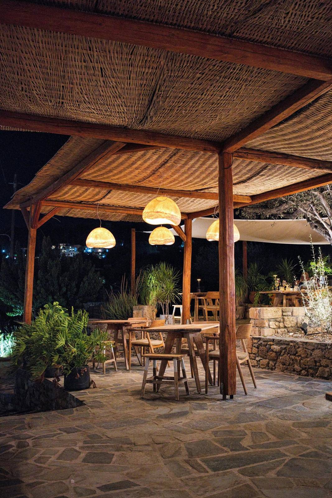 Kamena bašta restorana Žalfija navečer: stolovi pod pergolom sa lampama i kameni zid