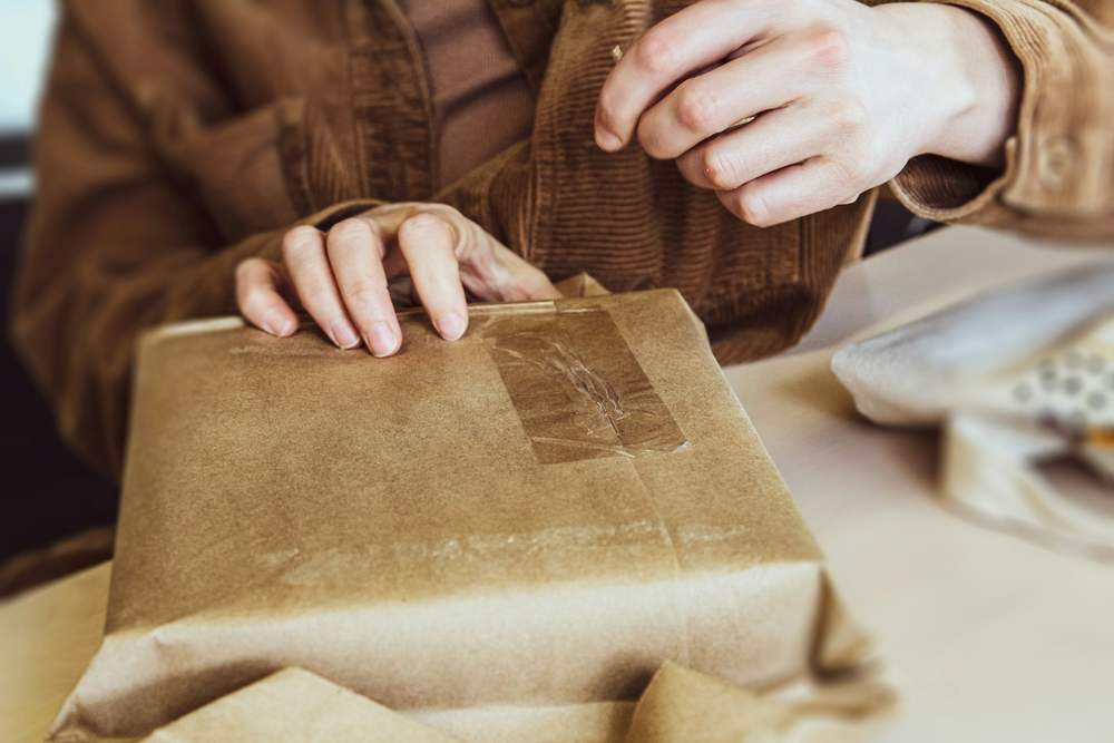 Ruke zatvaraju paket umotan u kraft papir na stolu u radionici
